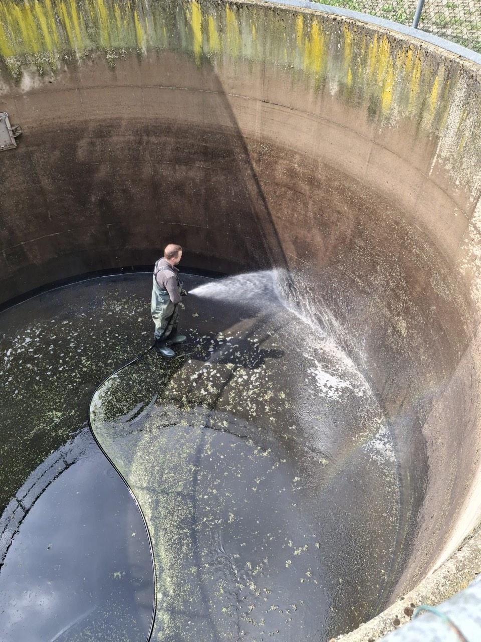 Techniker reinigt die Wand des Regenrückhaltebeckens mit dem Hochdruckschlauch